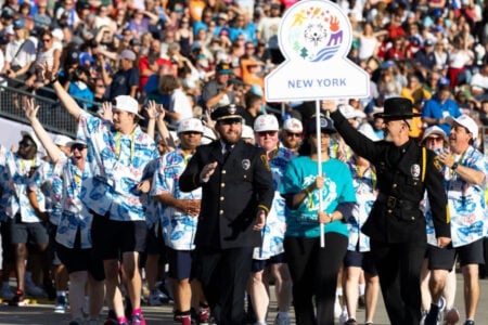 Team New York, including Special Olympics athletes and police, march in a parade, waving to a large crowd.