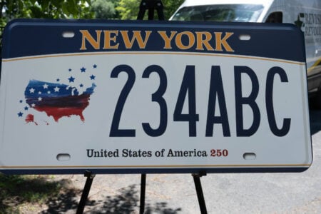New York's "United States of America 250" commemorative license plate, with a patriotic USA map, displayed outdoors.