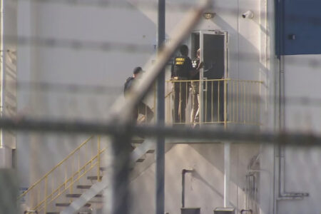 Federal agents at a building entrance; one stands on a landing, another walks up an outdoor metal staircase.