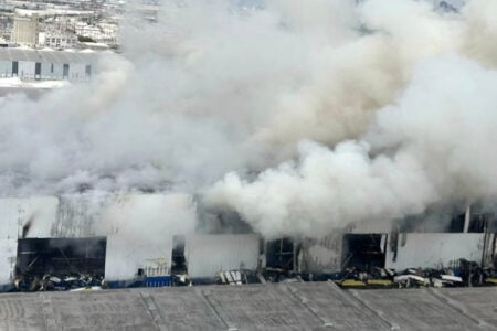 Large industrial building on fire, thick smoke billowing from its heavily damaged structure.