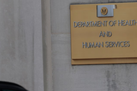 Gold sign for the US Department of Health and Human Services on a gray building wall.