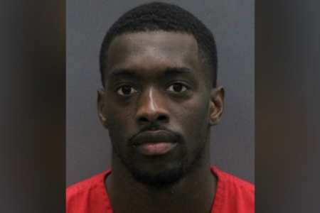 Mugshot of a young Black man with short dark hair, a beard, and a red uniform, looking at the camera.