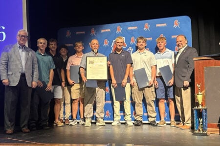 Seven Finger Lakes student-athletes and three officials stand on a stage with a proclamation and awards during a recognition ceremony.