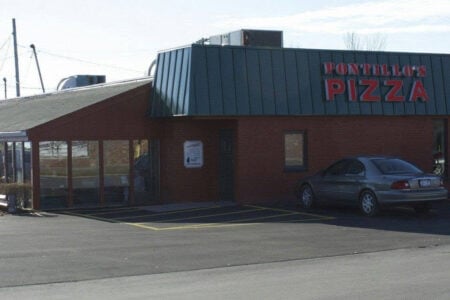 Exterior of Pontillo's Pizza building with red siding, green metal roof, glass windows, and a dark grey sedan in the parking lot.