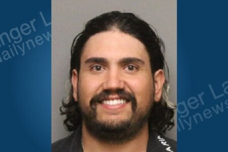 Mugshot of a smiling man with long dark hair, a mustache, and a full beard.