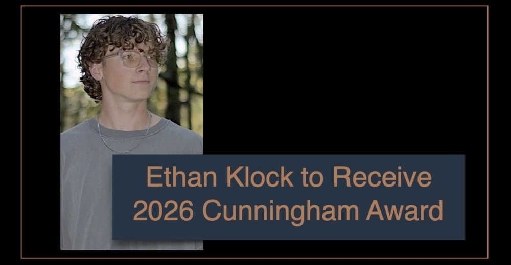 Young man Ethan Klock with curly hair and clear-framed glasses looks right outdoors against blurred foliage.