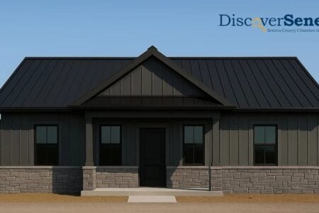 Modern dark gray house with black metal roof and stone foundation in a field under a blue sky, with the Discover Seneca logo.