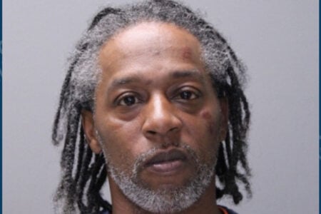 Mugshot of a Black man with graying dreadlocks and beard, looking forward, with marks on his forehead and left cheek.