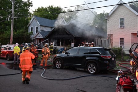 Syracuse firefighters battle a heavily smoking, charred house fire on a residential street.