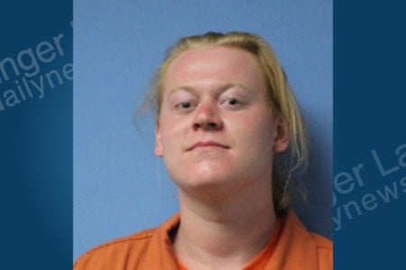 Mugshot of a person with blonde hair and fair skin wearing an orange uniform against a blue background.