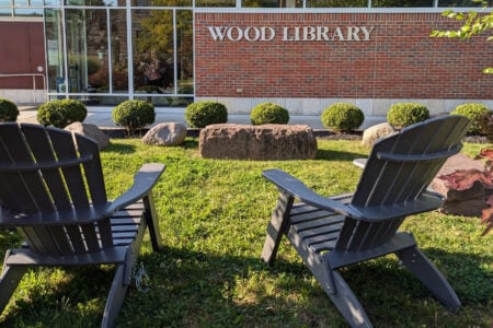 Two dark Adirondack chairs sit on a sunny lawn outside the Wood Library.