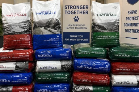 Stacked red, blue, green, and white bags of Diamond Naturals dog food for a community support drive.