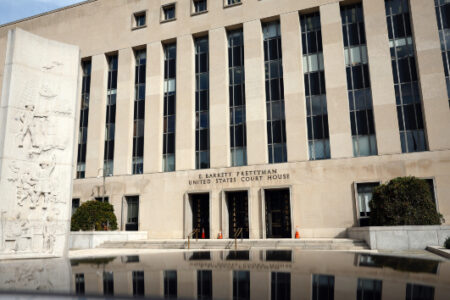 The E. Barrett Prettyman United States Court House, featuring a carved monument and its reflection in a foreground pool.