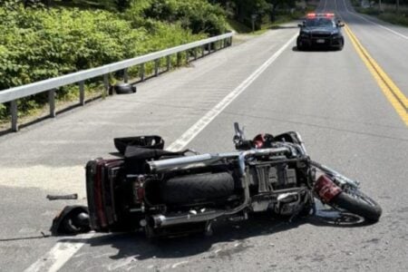Motorcycle lies overturned on a rural road with a police car in the distance.