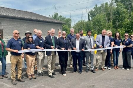 Community members and officials participate in a ribbon-cutting ceremony outside a gray brick building.