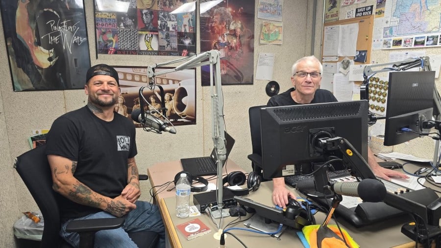 Two men in a radio studio: one in a 101.7 WALT shirt smiles; the other operates a sound console.