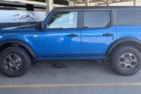 Blue Ford Bronco 4-door SUV parked next to a Greyhound bus in a parking lot.