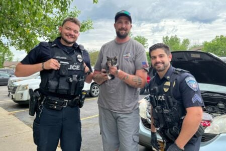 Two Seneca Falls Police officers and a man holding a rescued calico kitten smile in a parking lot.