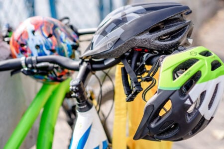 Assorted bicycle helmets, including green, black, and multi-colored, resting on bikes outdoors.