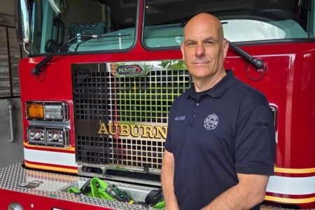 Firefighter Salvace in a navy polo shirt stands in front of a red Auburn Fire Department truck.