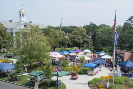 Crowds enjoy an outdoor festival with colorful tents on a town square, overlooked by a prominent courthouse with a golden dome.