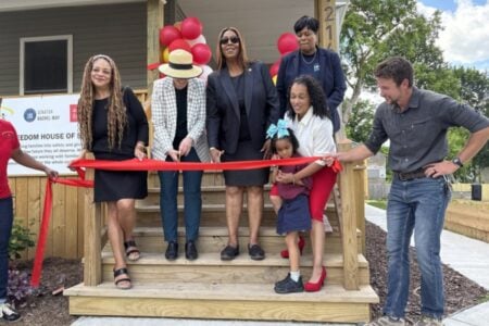 Community leaders and a child cut a red ribbon at the dedication of a new Freedom House home.