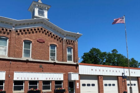Weedsport Village Office and Fire Department building with an American flag flying against a clear blue sky.