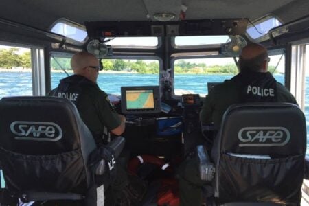 Two police officers pilot a patrol boat with navigation screens, cruising on a Finger Lakes waterway.