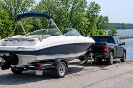 Black pickup truck backing a white and blue boat on its trailer down a paved boat ramp into a lake.