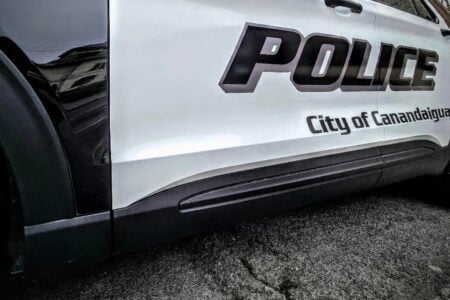 Side of a white and black City of Canandaigua police patrol vehicle with "POLICE" clearly visible, parked on asphalt.