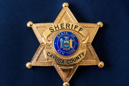 Gold six-point Sheriff's badge for Cayuga County, New York, with the state seal, on dark blue fabric.