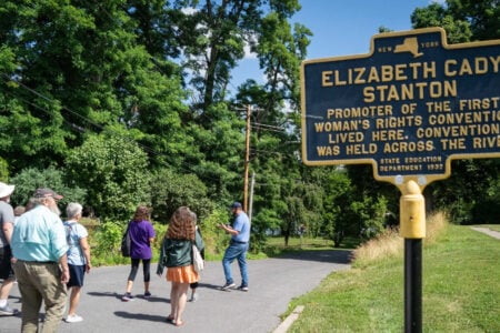 A historical marker for Elizabeth Cady Stanton, promoter of the first Women's Rights Convention, stands near a group of people on a path.
