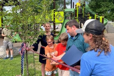 Children and adults cut a patriotic ribbon for a tree planting event at a local park playground.