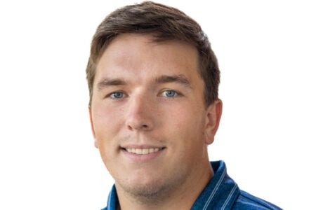 Smiling man with short brown hair and blue eyes, wearing a striped blue shirt against a white background.