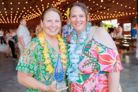 Dawn Shipman accepts a Seneca County Sustainability Supper Award with a smiling woman at a tropical indoor event.