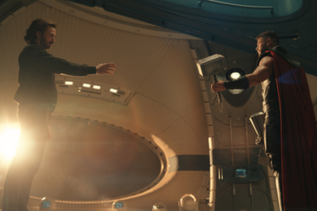 Tony Stark reaches out to Thor, who holds Mjolnir, inside a futuristic, curved chamber bathed in golden light.