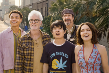 A diverse group of five people look up with expressions of awe on a sunny city street lined with palm trees.