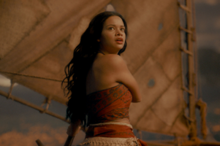 Young woman with dark hair and red top looks startled on a sailing boat with a large brown sail.