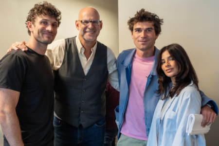 Four smiling people, three men and a woman, pose indoors against a light-colored wall.