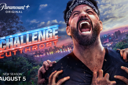 Bearded man in bandana screaming intensely as hands tear his shirt, overlooking a city skyline at dusk.