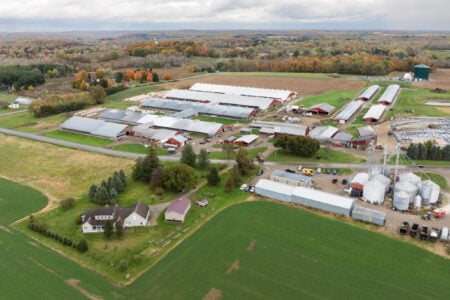 Aerial view of a large Finger Lakes dairy farm with numerous barns, silos, fields, and autumn foliage under a cloudy sky.