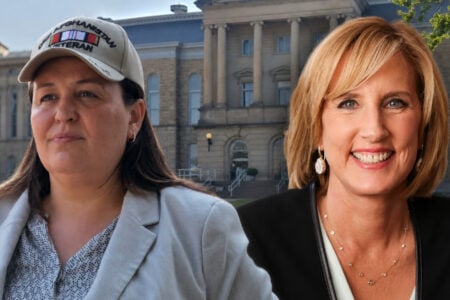 Woman in 'Afghanistan Veteran' hat and smiling woman posed before a stone courthouse-like building.