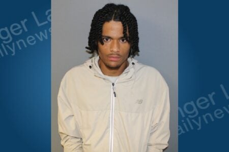 Mugshot of a young man with braided hair, wearing a tan hooded jacket, looking directly at the camera.
