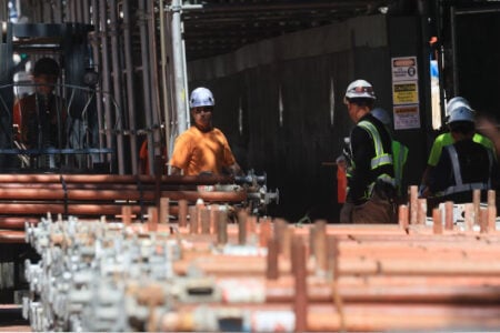 Construction workers use a forklift to move bundles of scaffolding poles at a job site.