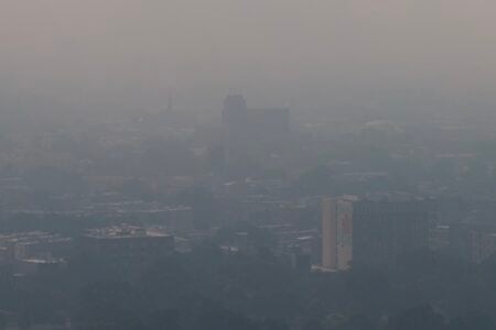 City skyline and buildings largely obscured by a thick, pervasive gray haze under a pale, overcast sky.
