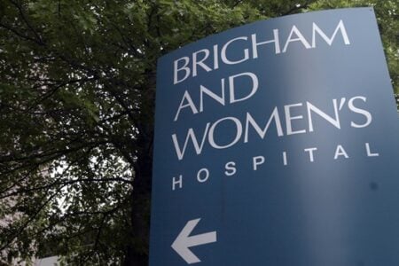 Brigham and Women's Hospital sign with an arrow, partially obscured by green tree leaves.