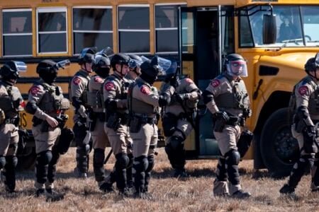Texas DPS officers in protective gear assemble near a school bus in a dry field.