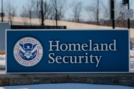 Blue U.S. Department of Homeland Security sign with agency seal, outdoors in snow near a road.