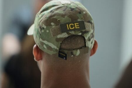 Back of a person's head wearing a camouflage cap with an "ICE" patch.