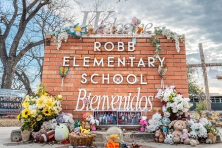 Robb Elementary School brick sign adorned with flowers, stuffed animals, and student photos, honoring victims.